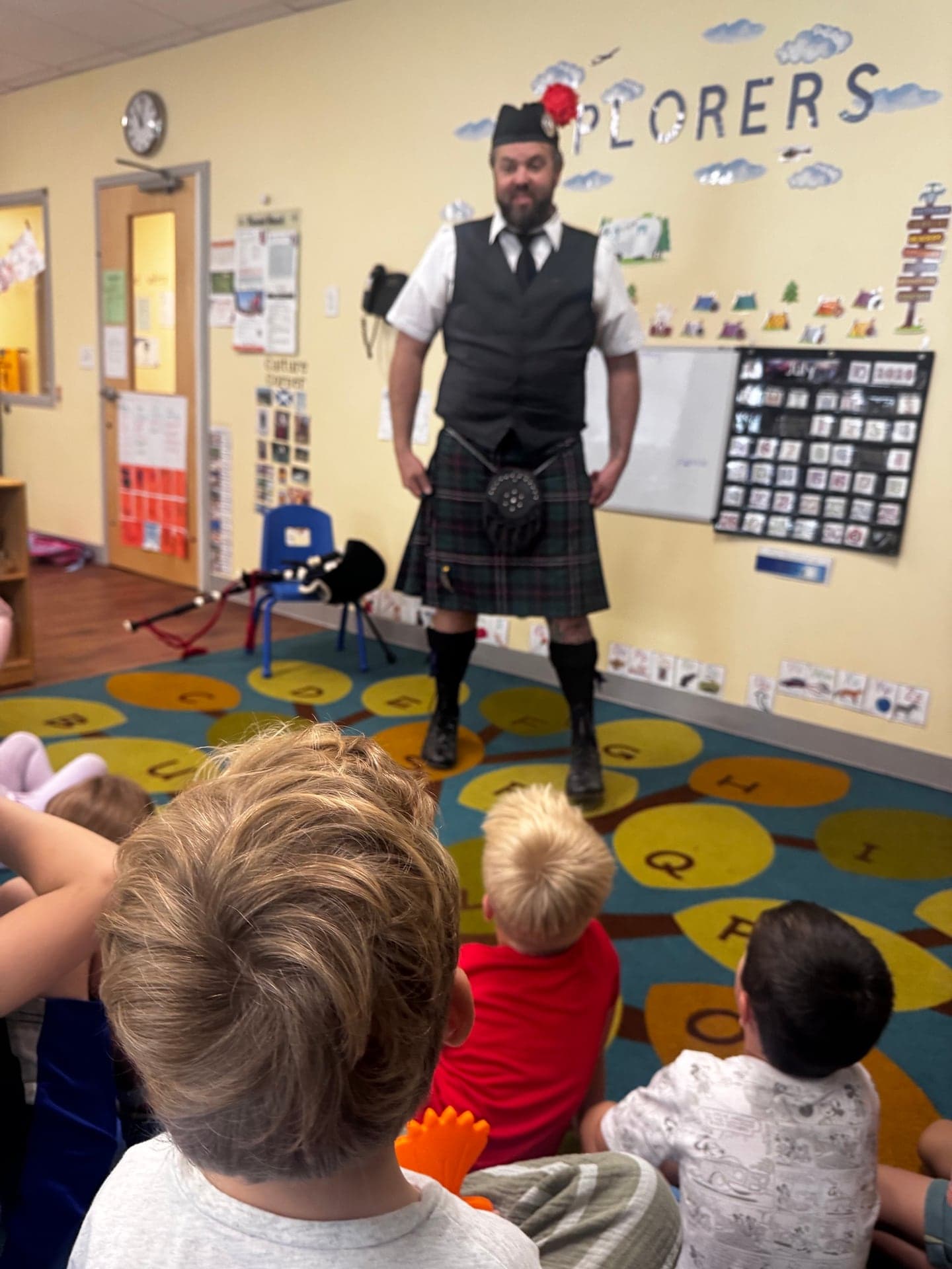 Ryan Guthrie introducing Highland bagpipes to a classroom while students listen from the floor