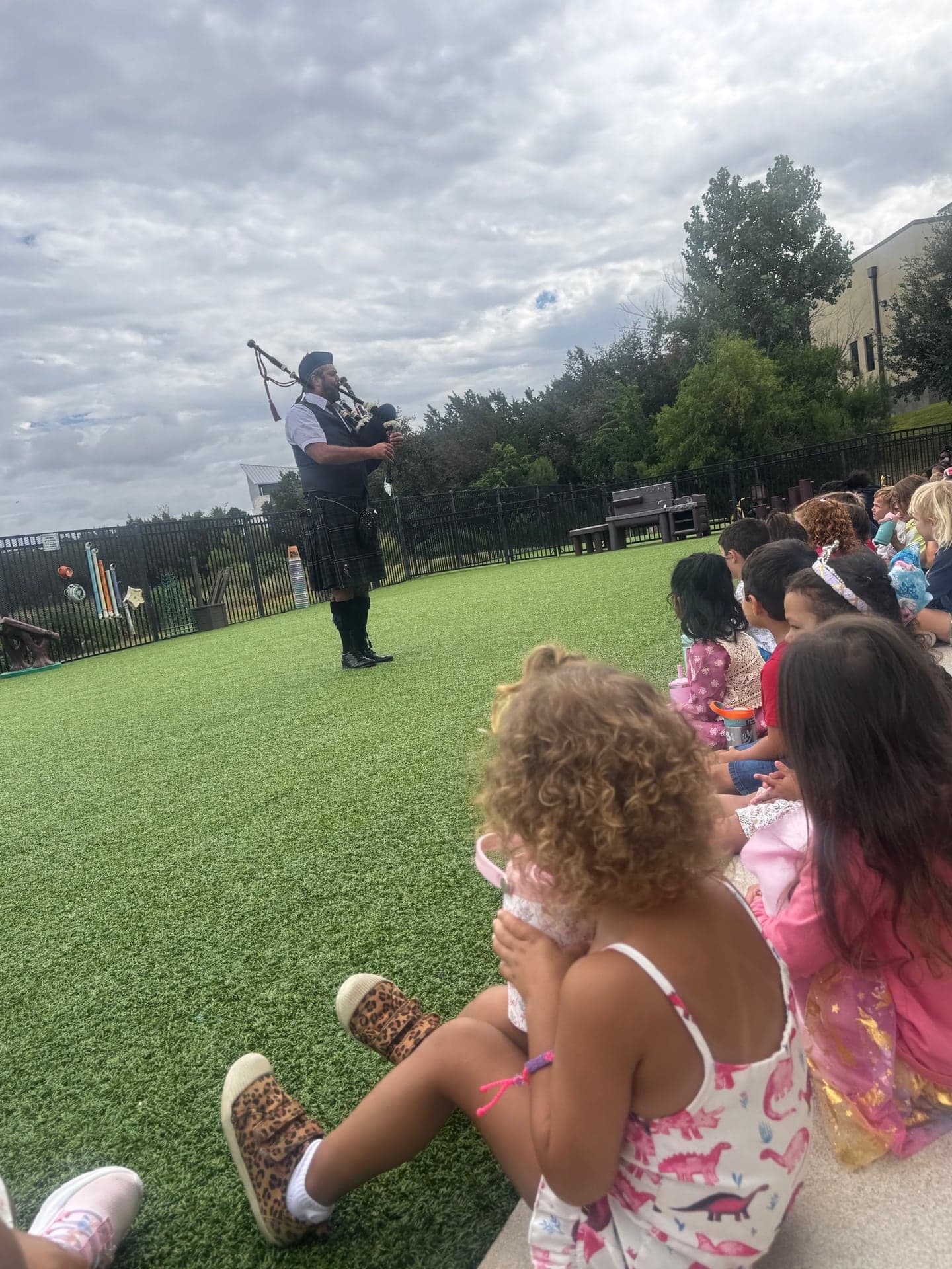 Students watching Ryan Guthrie perform Highland bagpipes in an outdoor school play area