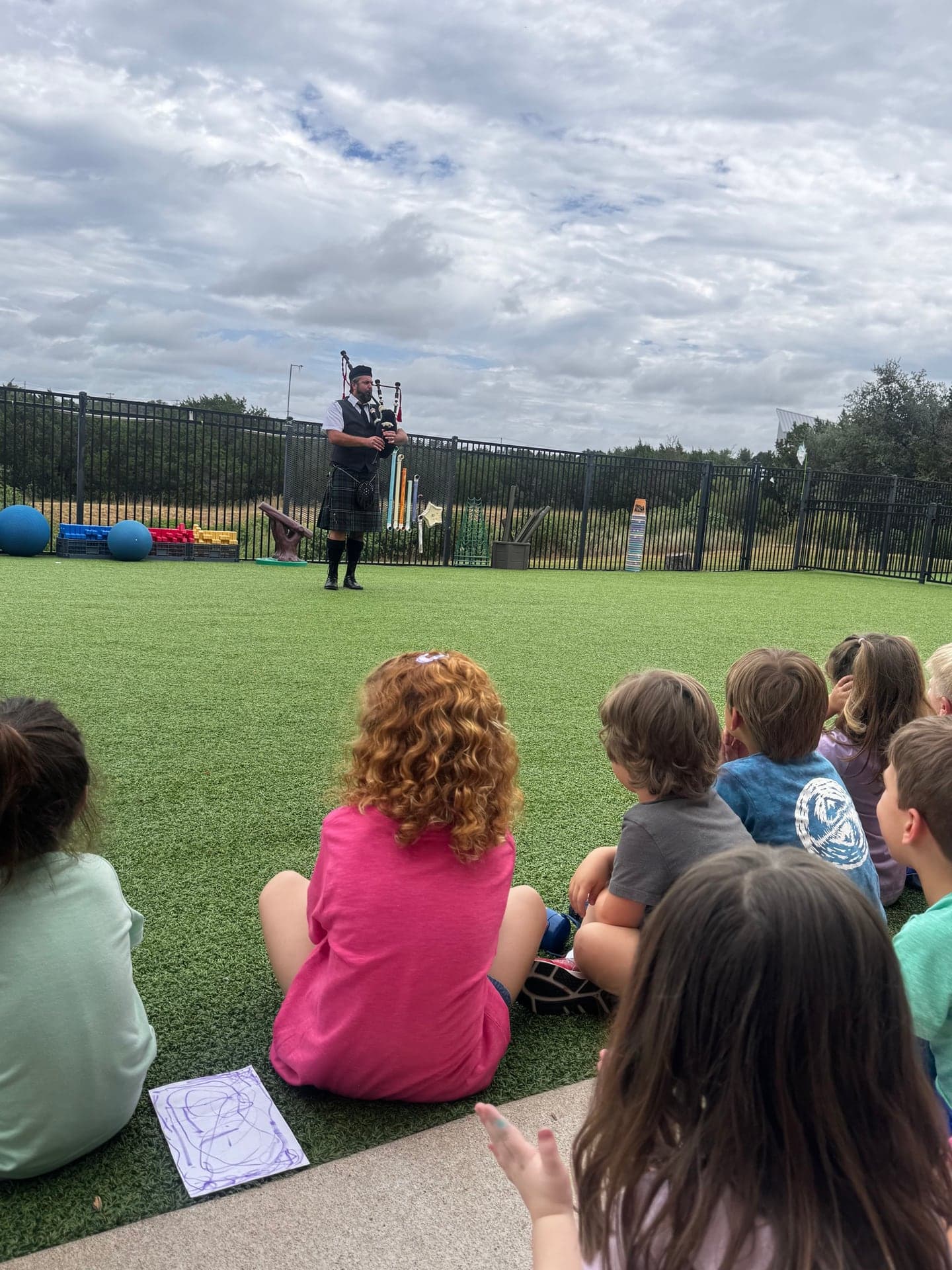 Ryan Guthrie performing Highland bagpipes outdoors for a seated school group